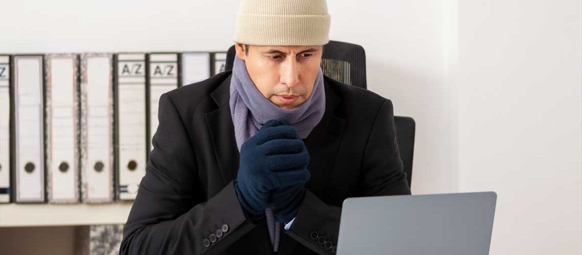 Worker bundled up in front of their computer on a cold day in the office